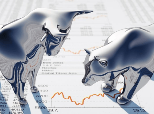 Chrome bear and bull statues standing on top of a printout of numbers and graphs.