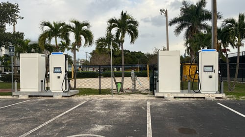 Several EVgo fast-charging units installed in marked parking spaces at a public charging station, with EVgo logos on the chargers, protective bollards around each unit
