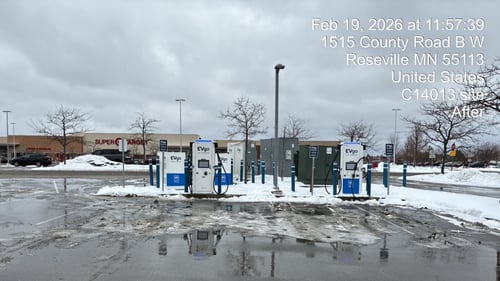 Several EVgo fast-charging units installed in marked parking spaces at a public charging station, with EVgo logos on the chargers, protective bollards around each unit
