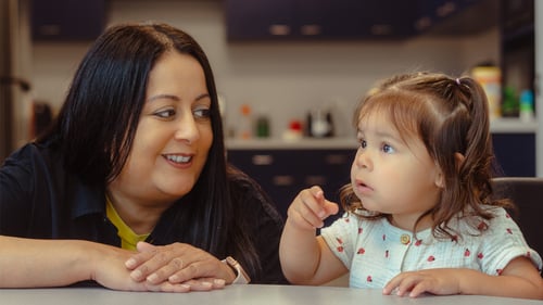 A caring ABA therapist smiling warmly at a young toddler who is pointing during an engaging early intervention autism therapy session.