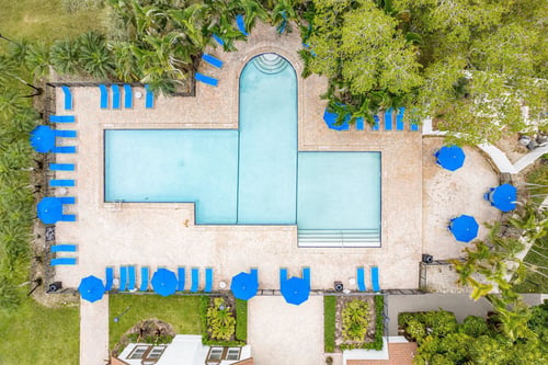 An aerial view of a pool surrounded by trees and blue umbrellas.