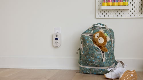 Kidde carbon monoxide detector on wall next to a child's backpack.