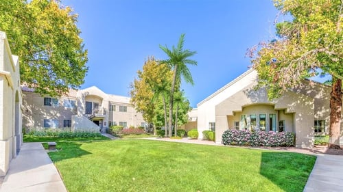Lush walkway between apartment buildings with balconies and green grass at Country Club at Valley View - 55+ Senior Community Apartments, Las Vegas