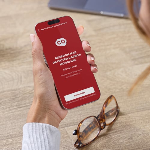 A woman holds a smart phone, showing a CO detection alert.