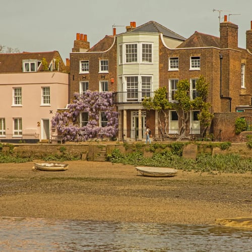 Knight Frank Chiswick Estate Agents - Historic brick houses along the River Thames at Strand-on-the-Green in London, shown at low tide with small boats.