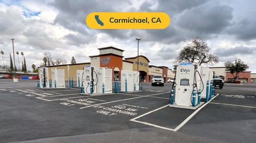 Several EVgo fast-charging units installed in marked parking spaces at a public charging station, with EVgo logos on the chargers, protective bollards around each unit