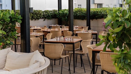 Restaurant seating area with wicker chairs, wooden tables set with glassware and lush greenery