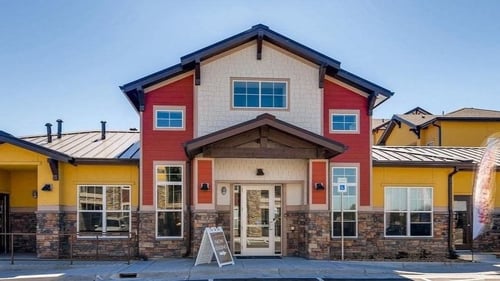 A building with a red and yellow facade has a white door and windows at Auburn Brook in Castle Rock, CO, 80109
