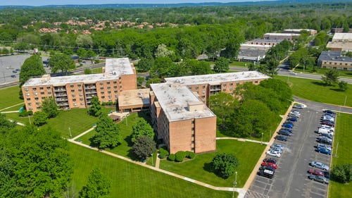 A parking lot is in front of a building with a green lawn in between at Menlo Manor Apartments, New Jersey, 08820
