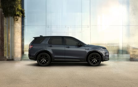 Side view of a grey Discovery parked in front of a modern glass building.