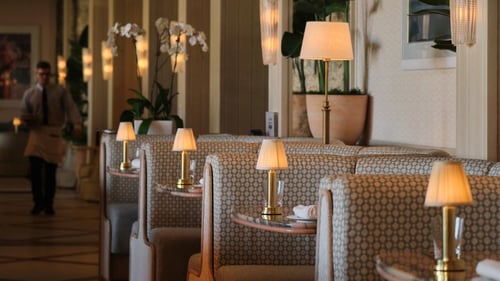 Elegant restaurant interior with upholstered booth seating, brass table lamps with white shades, white orchids, and warm ambient lighting.