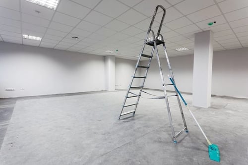 An empty room in a commercial commercial building with a large ladder prepared for wter damage restoration.