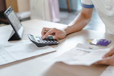 Person calculating expenses with calculator, tablet, credit cards, and financial documents on desk