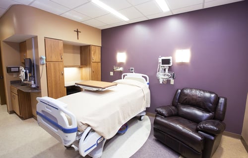 A view of a postpartum room showing a recliner, bed, storage and medical equipment.