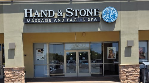 Clean exterior view of the Hand & Stone Massage and Facial Spa storefront on South Alma School Road in Chandler, Arizona, featuring prominent brand signage and a welcoming front entrance.