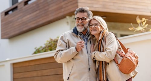 Retired couple standing by their family cottage, representing multi‑generation estate planning
