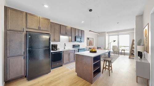 A modern kitchen with wooden cabinets and a black refrigerator at The Rosalyn in Bloomington, MN