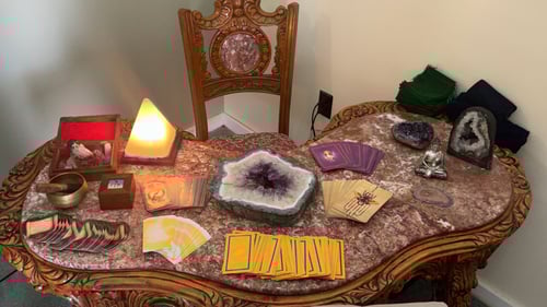 A very nice wood table with marble top covered with tarot cards, amethyst stones, and a singing bowl.