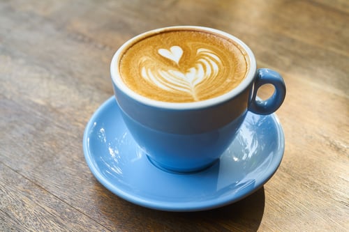 A close-up of a morning latte with heart-shaped latte art in a blue ceramic cup and saucer on a wooden table — header image for RBC Wealth Management's Our Monthly Morning Coffee.