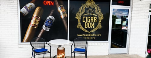 Front exterior of Cigar Box, a premium tobacconist featuring a welcoming storefront, branded window graphics, outdoor seating, and a clean, inviting entrance. This photo highlights the retail storefront and customer experience for local business listings.
