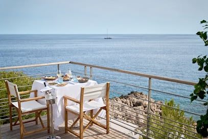 Club Dauphin overlooking the sea, featuring an outdoor swimming pool, lounge chairs, shaded seating areas, lush greenery and a hill in the background