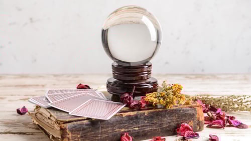 A psychic's crystal ball sits on top of an old book with tarot cards and dried flowers.