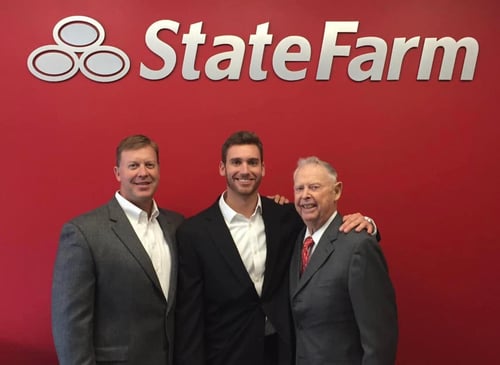 Agent Kyle with two other men dressed in suits, standing in front of red State Farm wall