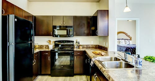 a kitchen with dark wood cabinets and stainless steel appliances at Villa Espada Apartments, San Antonio, TX