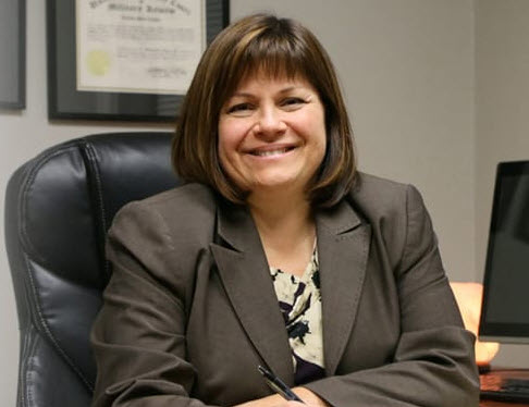 Attorney Katrina Luedtke wearing a gray suit sitting a desk smiling.
