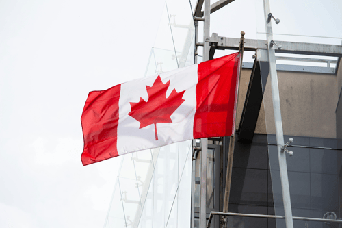 The Canadian flag billowing beside a building.