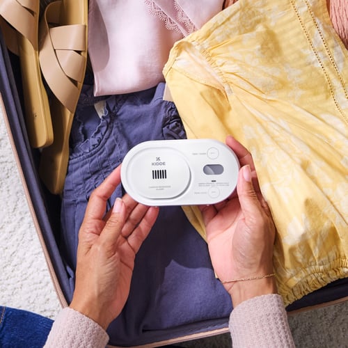 A person holds a CO detector over clothes in a suitcase.