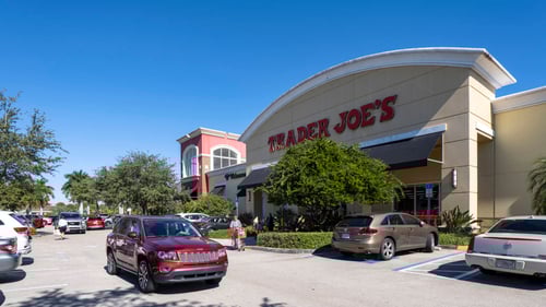 Red SUV driving past tree lined entrance of Trader Joe's