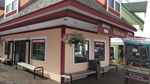 Exterior of the Kilwins Mackinaw City, MI 49701 chocolate, fudge, and ice cream store with benches out front for sitting