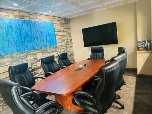 Brown conference table with black chairs surrounding and tv hanging on the wall
