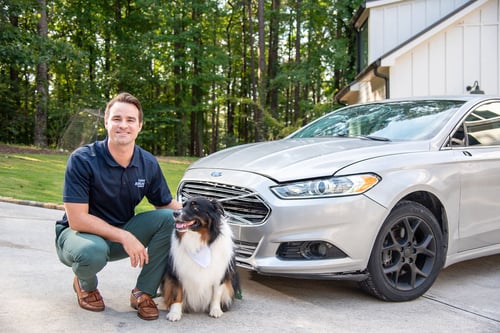 A Georgia Farm Bureau Insurance Agent poses in front of a home and a vehicle with the company's mascot