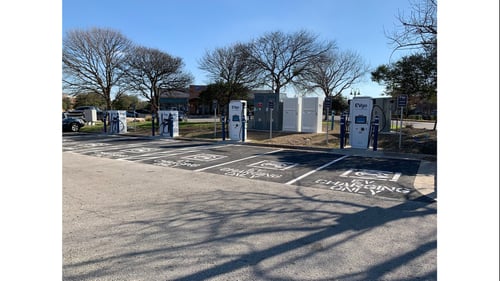 Several EVgo fast charging units installed in marked parking spaces at a public charging station, with EVgo logos on the chargers, protective bollards around each unit.