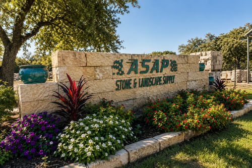 ASAP Stone & Landscape Supply entrance sign in Austin, TX with limestone wall, colorful flower beds, and landscaped stone border.