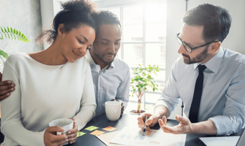 A group of individuals in a meeting, discussing documents, with coffee cups on the table and a plant in the background.