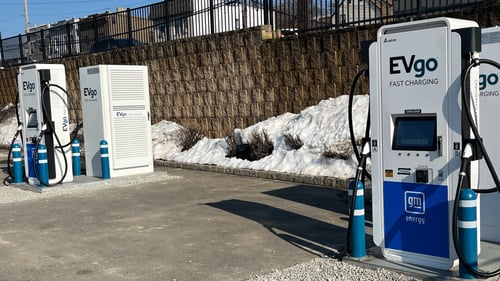 Several EVgo fast-charging units installed in marked parking spaces at a public charging station, with EVgo logos on the chargers, protective bollards around each unit