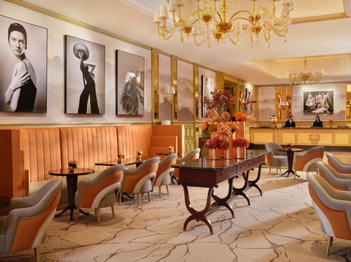 Il Salotto interiors features pastel orange, taupe, and cream-colored chairs with mirrored glass surfaces and large paintings hanging on the walls. A reception area is visible in the background.