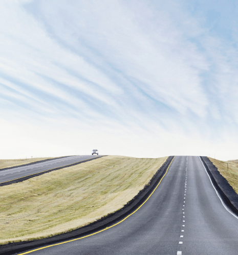A car coming down a grass led road, with a cloudy blue sky in the background.