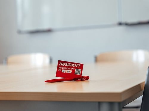 Beispiel Unterrichtsraum vor Ort mit Tisch, Stühlen und White Board an der Wand.
