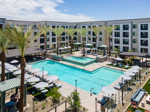 Aerial view of a pool with lounge chairs, umbrellas, cabanas, and palm trees.