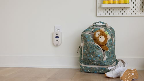 Picture of an Indoor Air Quality Monitor next to a kid's backpack.