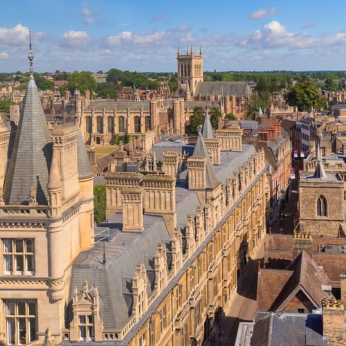 Knight Frank Cambridge Estate Agents - High-angle architectural view of historic stone buildings and spires of Gonville & Caius College in Cambridge, England, under a partly cloudy sky.