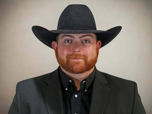 A man in a black cowboy hat and suit stands against a neutral background, exuding a confident and professional demeanor.