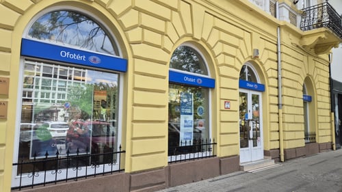 Ofotért optikai üzlet sárga, díszes homlokzatú épületben, íves kirakatokkal Szolnok belvárosi utcáján.