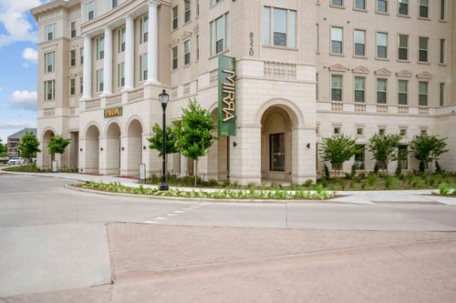 Exterior of a light brick building with arched entrances and white columns with a vertical sign that says "Mirra".