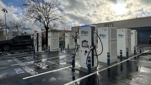 Several EVgo fast-charging units installed in marked parking spaces at a public charging station, with EVgo logos on the chargers, protective bollards around each unit
