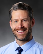 Samuel Doniach, APRN, CRNA smiling in front of a gray background.